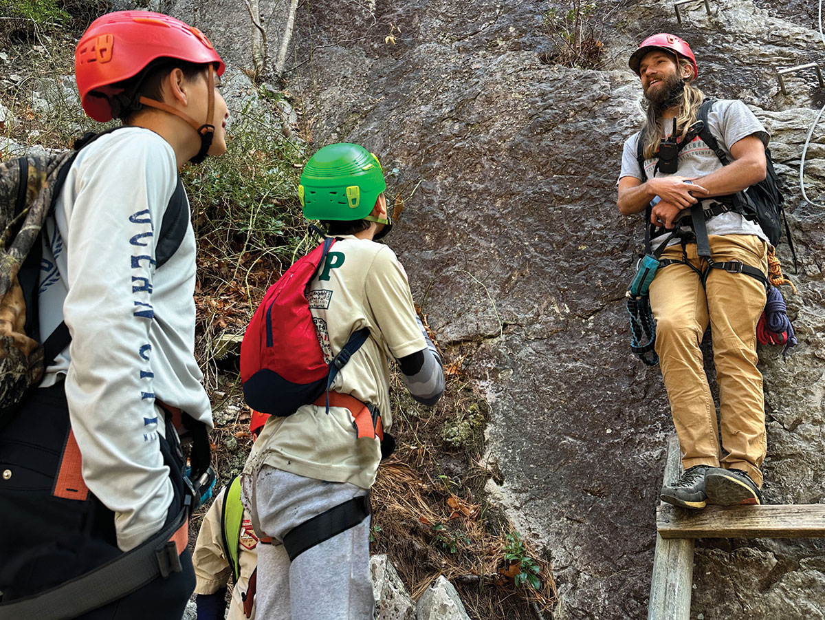 Dois escoteiros recebem instruções de um gerente de escalada do NROKS