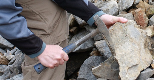 man holds a pick next to a rock