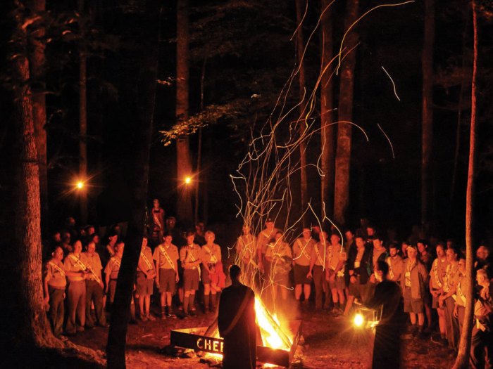 Order of the Arrow members standing around a campfire