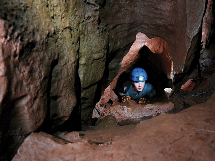 Scout crawling through a tight passage during a cave exploration